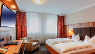 Doppelzimmer Comfort, helles Holz und orangene Vorhänge mit Blüten.