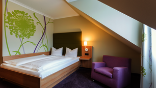 Doppelzimmer Comfort Smart, lila und grün mit Pusteblume-Tapete. Das Bett steht an der Wand.