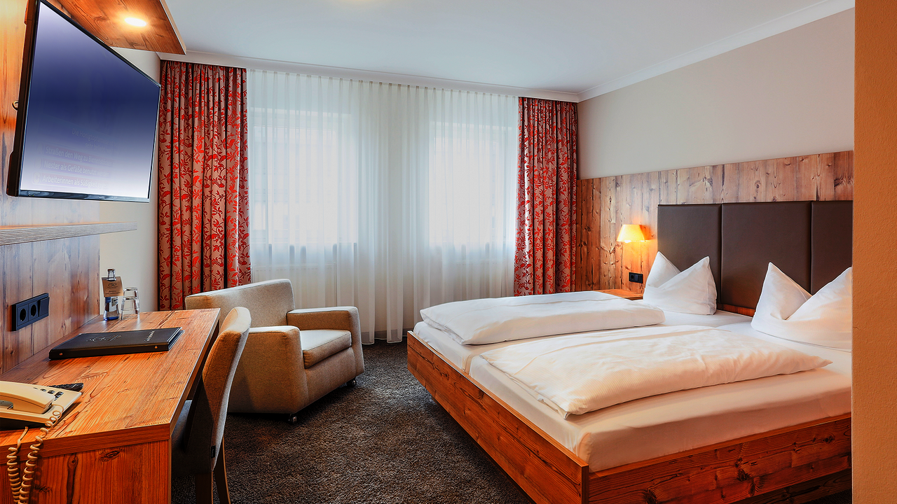 Doppelzimmer Comfort mit hellem Holz und orangenen Vorhängen mit Blüten